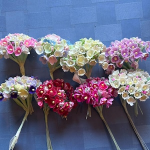 May include: Assortment of ten bunches of artificial flowers, each bunch containing approximately 20 small paper flowers. The flowers are in various shades of pink, purple, white, and light blue.