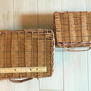 May include: Two woven wicker baskets, one rectangular and one square, with handles. The larger basket measures approximately 12 inches in length. Both baskets are a light brown color and appear to be vintage.