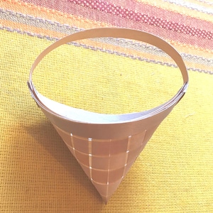 May include: A conical metal coffee filter featuring a fine mesh grid pattern throughout its structure. The filter has a wide, circular top rim and a narrow, pointed base, designed with a thin, curved handle attached to the upper edge for easy handling.