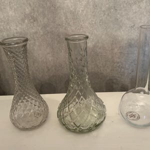 May include: Three clear glass vases of varying shapes. Two vases feature a textured diamond pattern across their bulbous bodies and narrow necks. The third vase has a smooth, spherical base and a tall, slender, cylindrical neck.
