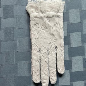 May include: A pair of white lace gloves with a delicate floral pattern. The gloves have a ruffled edge at the wrist.