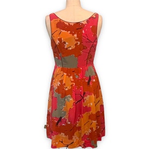 K&ouml;nnte beinhalten: Ein &auml;rmelloses, knielanges Kleid mit einem farbenfrohen abstrakten Druck in Orange-, Rosa- und Graut&ouml;nen. Das Kleid hat einen figurbetonten Oberteil und einen flie&szlig;enden Rock.
