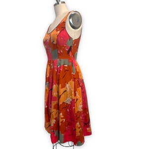 K&ouml;nnte beinhalten: Ein &auml;rmelloses Kleid mit einem abstrakten Druck in Rosa, Orange und Braun. Das Kleid hat einen figurbetonten Oberteil und einen vollen Rock.