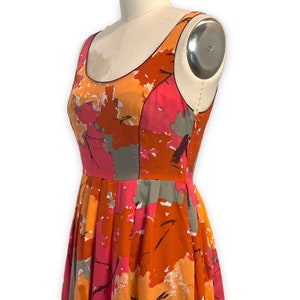 K&ouml;nnte beinhalten: Ein &auml;rmelloses Kleid mit einem abstrakten floralen Druck in Rosa, Orange und Grau. Das Kleid hat einen taillierten Oberteil und einen vollen Rock.
