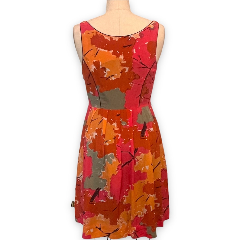 K&ouml;nnte beinhalten: Ein &auml;rmelloses, knielanges Kleid mit einem farbenfrohen abstrakten Druck in Orange-, Rosa- und Graut&ouml;nen. Das Kleid hat einen figurbetonten Oberteil und einen flie&szlig;enden Rock.
