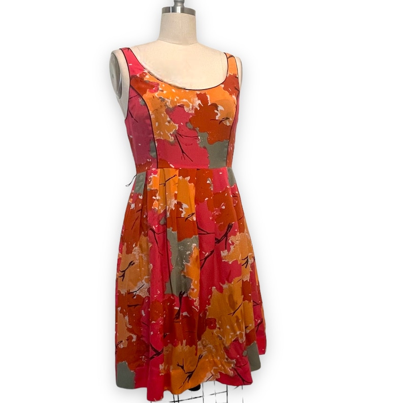 K&ouml;nnte beinhalten: Ein &auml;rmelloses Kleid mit floralem Druck in Rosa, Orange und Grau, mit einem taillierten Oberteil und einem weiten Rock.