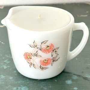 May include: White ceramic pitcher with a floral design featuring pink flowers and brown stems. The pitcher has a handle and a smooth, white glaze.