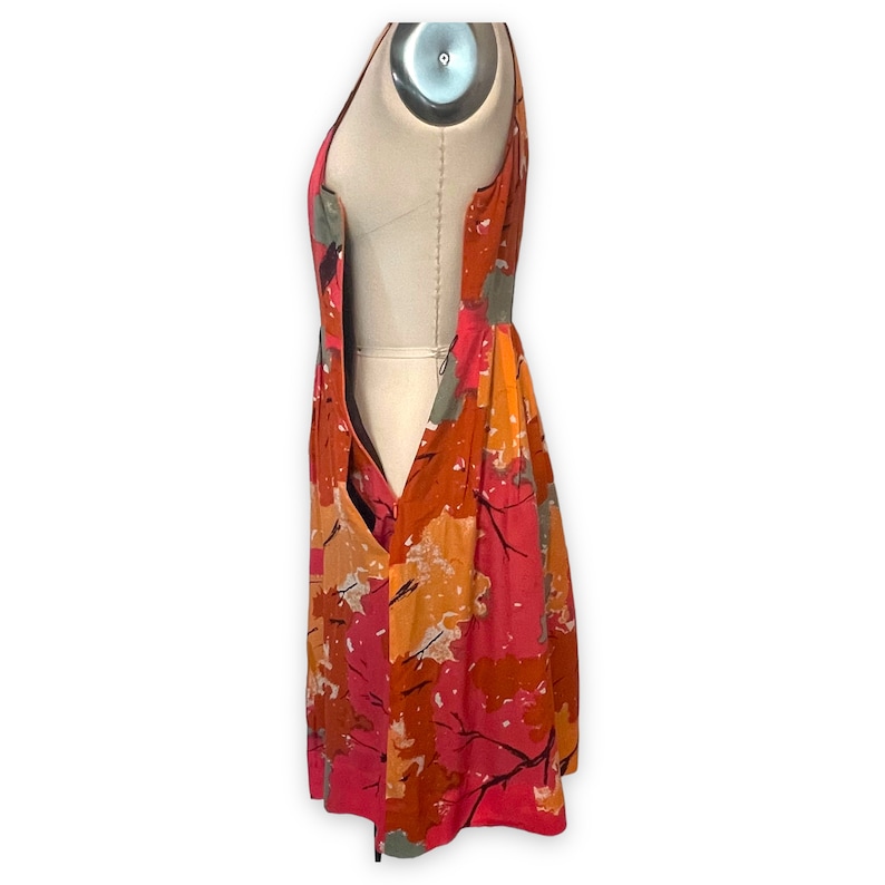 K&ouml;nnte beinhalten: Ein &auml;rmelloses Kleid mit einem abstrakten Druck in Rosa, Orange und Grau. Das Kleid hat einen figurbetonten Oberteil und einen flie&szlig;enden Rock.