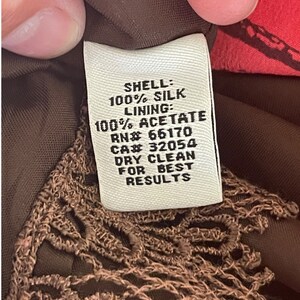 K&ouml;nnte beinhalten: Ein wei&szlig;es Etikett mit schwarzem Text, das die Stoffzusammensetzung eines Kleidungsst&uuml;cks beschreibt. Das Etikett lautet "SHELL: 100% SILK LINING: 100% ACETATE RN# 66170 CA# 32054 DRY CLEAN FOR BEST RESULTS".