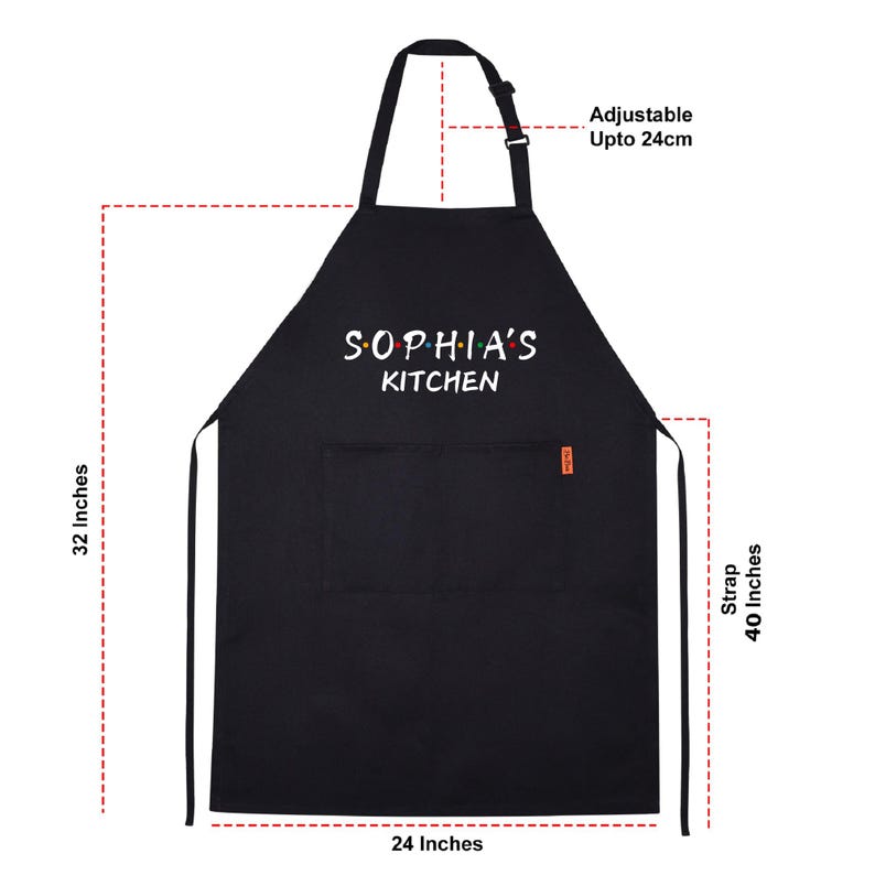 Puede incluir: Delantal de cocina negro con tirantes ajustables. El delantal tiene un bolsillo y dice "Sophia's Kitchen" en texto blanco con puntos de colores.