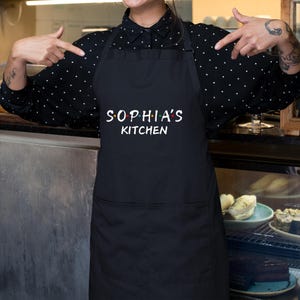 Puede incluir: Delantal negro con texto blanco que dice "Sophia's Kitchen".