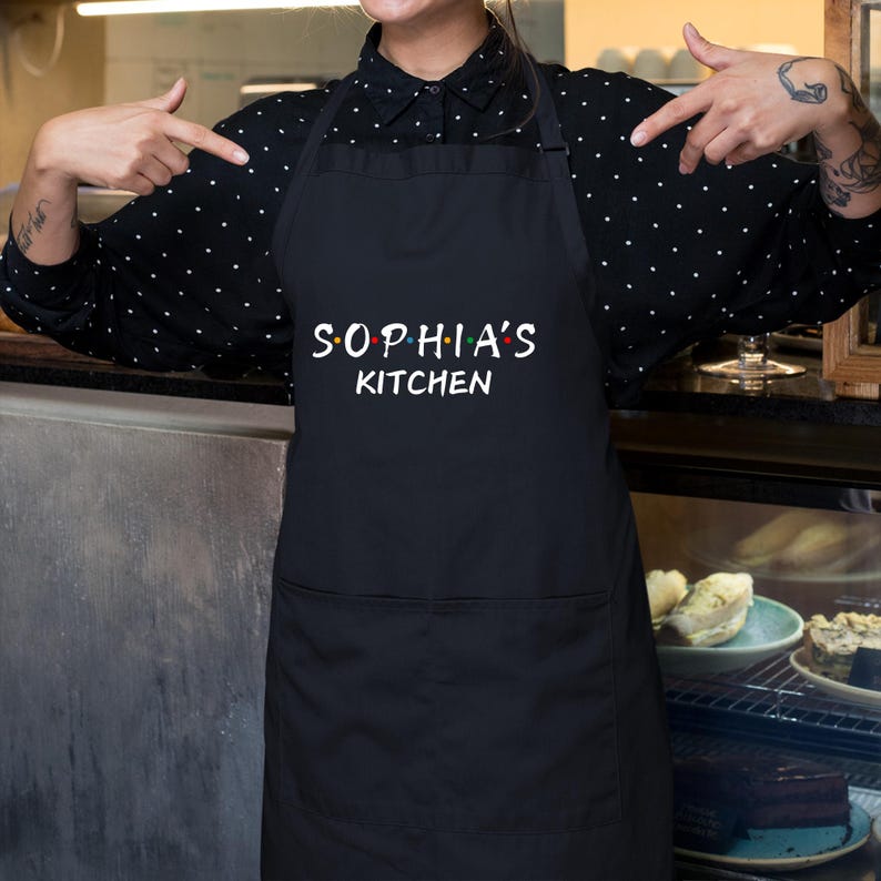 Puede incluir: Delantal negro con texto blanco que dice "Sophia's Kitchen".