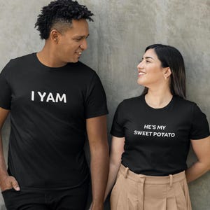 Pode incluir: Um casal usando camisetas pretas combinando com uma mensagem divertida sobre comida. A camiseta do homem diz "I YAM" e a camiseta da mulher diz "He's my sweet potato".