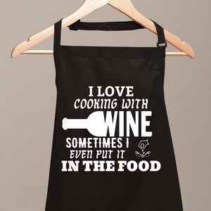 Puede incluir: Delantal de cocina negro con texto blanco que dice "Me encanta cocinar con vino, a veces incluso lo pongo en la comida". El texto está acompañado por un gráfico de una botella de vino y una mano vertiendo vino.