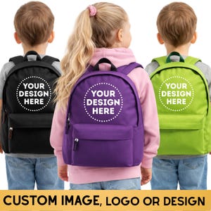May include: Three backpacks in black, purple, and lime green, each featuring a circular white dotted border and the text YOUR DESIGN HERE printed on the front pocket. The bags have a top handle, adjustable shoulder straps, and a front zipper.