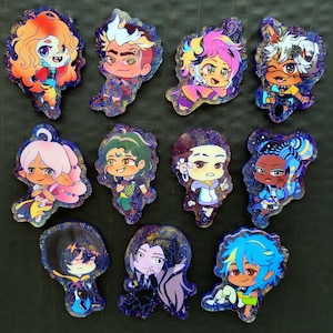 Puede incluir: Un conjunto de diez pines de personajes coloridos con fondos de purpurina. Los personajes están dibujados en un estilo de dibujos animados y presentan una variedad de peinados, ropa y accesorios.