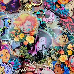 May include: A collection of colorful, iridescent, holographic character charms with keychains. The charms feature various characters with different expressions and hairstyles. Some charms have floral designs and others have star-shaped keychains.
