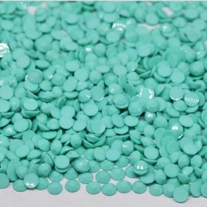 Op de afbeelding: Een close-up van een stapel turquoise, ronde, gefacetteerde harskralen. De kralen zijn verspreid en vullen het frame. De kralen zijn voor diamond painting.