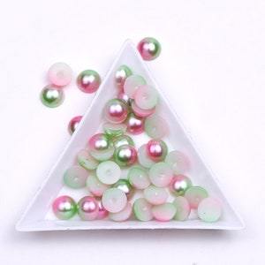 May include: A white triangular dish filled with green and pink iridescent round beads. The beads are arranged in a random pattern.