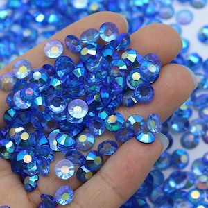 May include: A hand holding a pile of small, round, blue iridescent rhinestones.