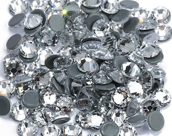 May include: A large pile of clear glass rhinestones with silver backs. The rhinestones are scattered on a white surface.