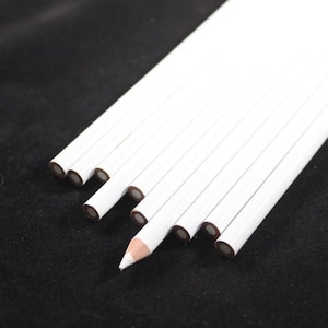 Puede incluir: Un grupo de lápices de marcar blancos con puntas marrones. Los lápices están dispuestos en forma de abanico, con un lápiz apuntando hacia la parte inferior de la imagen.