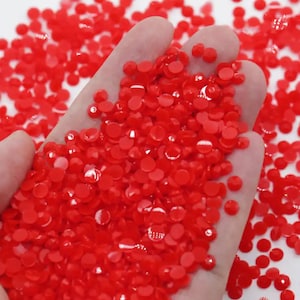 May include: A close-up of a hand holding a large quantity of small, bright red, round rhinestones.