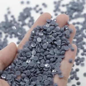 May include: A hand holding a large quantity of small, round, gray rhinestones. The rhinestones have a slightly iridescent finish.