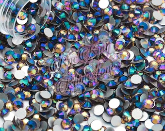 May include: A close-up image of a large quantity of iridescent blue and gold rhinestones. The rhinestones are scattered on a white surface.