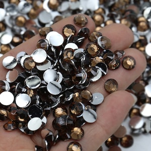 May include: A hand holding a large quantity of small, round, brown rhinestones with silver backs.