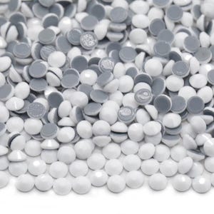 Puede incluir: Un montón de piedras de imitación redondas autoadhesivas blancas con un respaldo adhesivo gris.