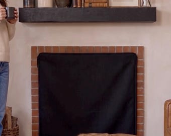 May include: A black rectangular fireplace cover made of fabric, positioned over a brick fireplace opening. The cover features a simple, flat design with a dark border, serving as a screen to block the hearth area while a golden dog rests nearby.