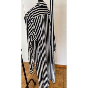 May include: A long-sleeved shirt with vertical black and white stripes. The shirt has a collar and button closure.