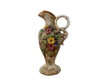 May include: A ceramic pitcher with a floral design. The pitcher is beige with gold accents and features a variety of colorful flowers.