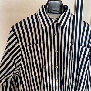 May include: A long-sleeved, striped shirt with a white and navy blue pattern. The shirt has a button-up front and a collar. The shirt has two pockets on the front.