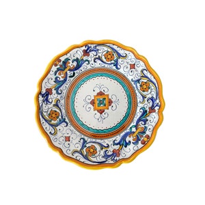 Puede incluir: Un plato de cerámica blanco con un borde festoneado y un diseño floral colorido. El diseño presenta colores azules, verdes, naranjas y amarillos.