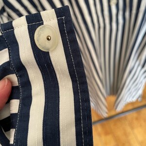 May include: Close-up of a white button with a gold center, sewn onto a blue and white striped fabric.