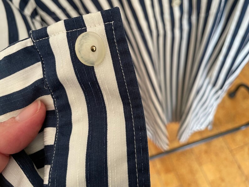 May include: Close-up of a white button with a gold center, sewn onto a blue and white striped fabric.