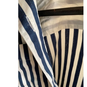 May include: Close-up of a blue and white striped shirt collar. The shirt has a button closure and a white lining.
