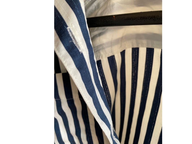 May include: Close-up of a blue and white striped shirt collar. The shirt has a button closure and a white lining.
