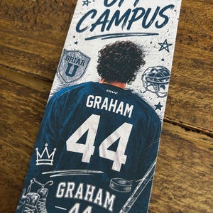 Op de afbeelding: Blauw en witte bladwijzer met de tekst "OFF CAMPUS" en een hockeythema. De bladwijzer toont een hockeytrui met de naam "GRAHAM" en het nummer "44". Extra afbeeldingen zijn een hockeyhelm, schaatsen en een hockeystick.