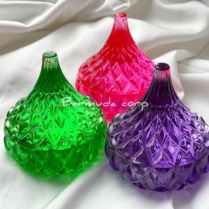 Puede incluir: Tres platos de dulces decorativos de vidrio con forma de beso de Hershey. Los platos son verdes, rosas y morados.