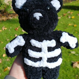 May include: Black plush teddy bear with a white skeleton design. The bear has a white nose and white eyes.