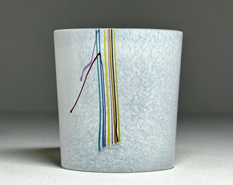 Puede incluir: Un vaso de vidrio blanco con una superficie texturizada y rayas de vidrio de colores que corren verticalmente por el lado.