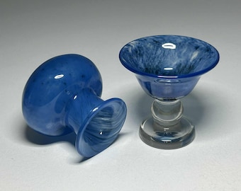 May include: Two blue glass goblets. One is upright, the other is on its side. The goblets have a clear stem and base, with a blue bowl. The blue bowl has a marbled white pattern.