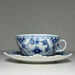 May include: A white teacup and saucer set with a blue floral design. The teacup has a delicate handle and sits on a matching saucer. The set is made of porcelain and is suitable for serving tea.