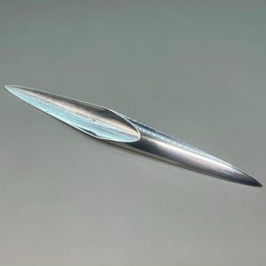 May include: A polished, silver-colored metal object with a long, tapered shape. The object has a hollow, boat-like interior and a pointed tip. The design is sleek and modern, with a reflective surface. The object is likely a decorative or functional item.