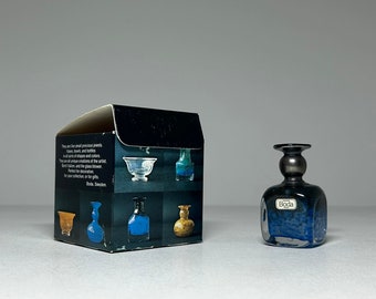 May include: A small, square, blue glass vase with a silver top and a "Boda" label. The vase is in a box with images of other glass vases.