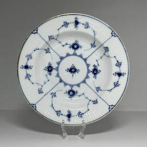 Puede incluir: Plato de porcelana blanca con un diseño floral azul. El plato tiene una textura acanalada y un borde dorado. El patrón azul presenta flores estilizadas y formas geométricas, que irradian desde el centro. Una pieza decorativa para servir o exhibir.