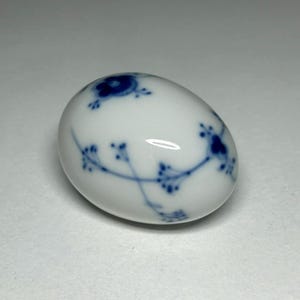 May include: White ceramic egg with blue floral pattern. The egg-shaped ornament has a glossy finish and delicate blue botanical designs. A decorative item for display or collection.